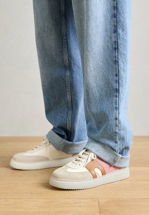 Weiße und beige Sneakers mit rosa und braunen Akzenten, ausgestattet mit einer glatten Oberfläche, Schnürverschluss und einer dicken weißen Sohle.