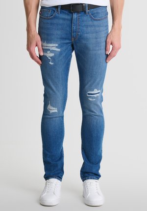 Sinine teksapüksid slim-fit lõikega, millel on mõlemal jalal ratastega detailid, tikkimisaktsendid ja vöökoht vöökinnitusloopidega.