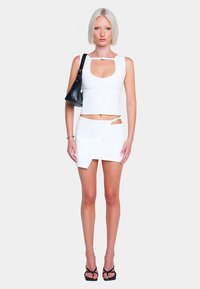 Ensemble composé d'un crop top blanc et d'une mini-jupe, avec un décolleté arrondi, un détail découpé et une fente latérale, assorti à des accessoires noirs et des talons.