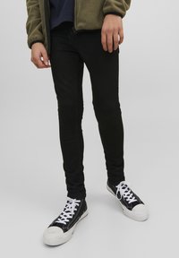 Jeans skinny noirs associés à des baskets noires et blanches. Les jeans ont une texture lisse, un design ajusté et un léger éclat.