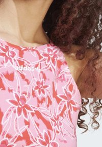 Różowy top na ramiączkach z kwiatowym wzorem w odcieniach czerwieni i bieli. Posiada logo Adidasa w bieli na dekolcie. Gładka tekstura materiału.