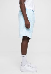 Lyseblå tie-dye shorts med elastisk talje og sidelommer, iført med hvide Nike-sokker og sneakers. Glat tekstur, afslappet design.