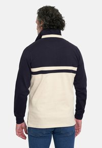 Camisa de manga larga con la parte superior en color azul marino y la sección inferior en color crema, adornada con una franja horizontal crema en la parte posterior. Material de algodón.