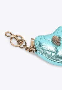 Borsa metallica turchese a forma di cuore con texture trapuntata, catena dorata e chiusura, con un motivo decorativo a conchiglia dorata sul fronte.