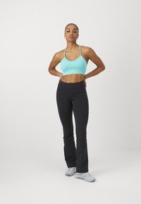 Turquoise sports bra and black flared leggings with smooth texture. Athletic style with minimal branding. Shoes in light blue/grey.