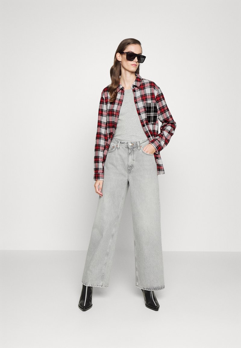 Czerwona i czarna flanelowa koszula w kratę na szarym t-shircie, w połączeniu z jasnoszarymi spodniami typu wide-leg i czarnymi, spiczastymi botkami za kostkę.