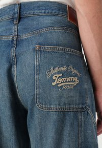Plave traperice s stražnjim džepom na kojem je izvezeno "Authentic Original Tommy Jeans" u krem boji. Uključeno klasično šivanje i kožna oznaka.