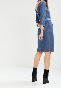 Denim-asuste, jossa on napakka, keskipitkä hame ja lyhyt, pitkähihainen paita, jossa on matala selkäosa. Tumansiniset värit kuluneilla reunoilla.