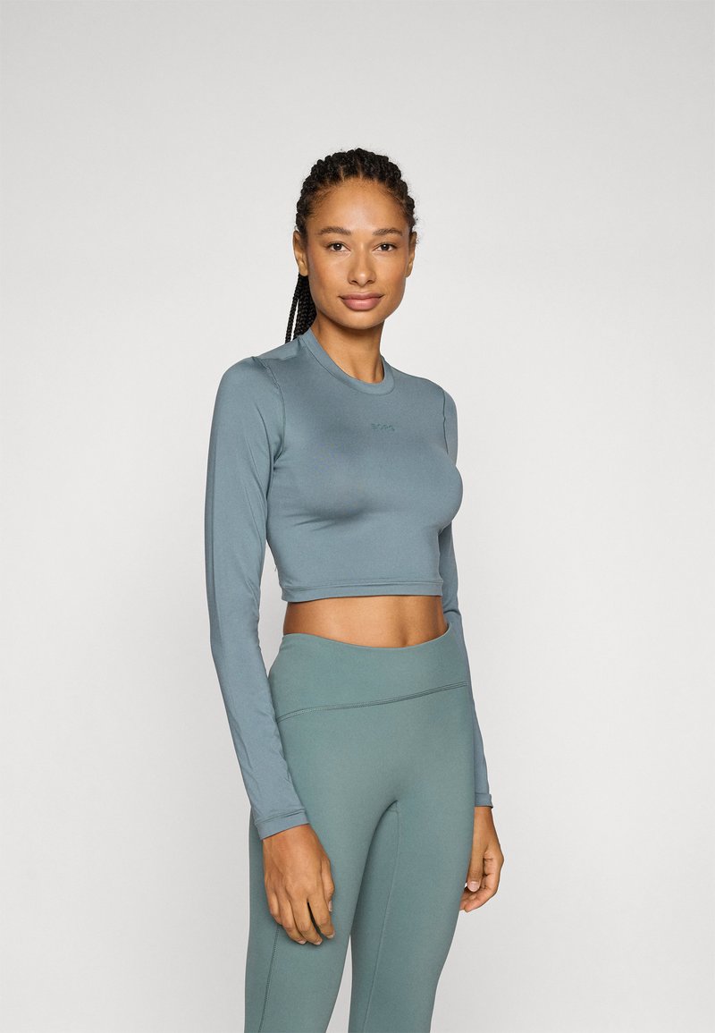 Ljusblå långärmad crop top och matchande högmidjade leggings, båda i ett mjukt, elastiskt material. Diskret logotypdetalj på toppen.