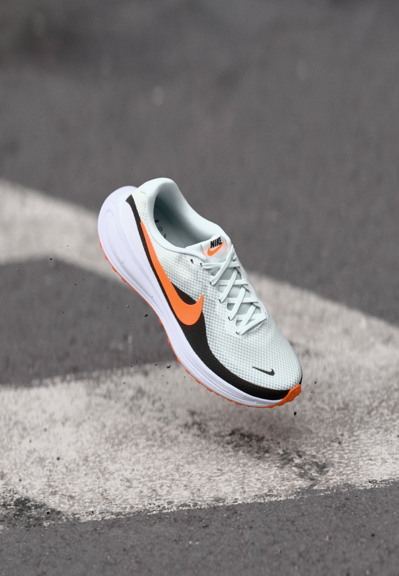 Chaussure de course en mesh bleu clair avec des accents noirs et orange vif. Elle possède une semelle blanche amortie et des lacets. Logo Nike visible.