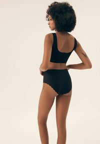 Czarny bezszwowy zestaw biustonosza i majtek o wysokim stanie. Góra ma szeroki dekolt, a dół charakteryzuje się falbaniastym wykończeniem. Gładka tekstura.