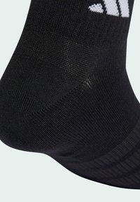 Czarna skarpetka wykonana z teksturowanego dzianinowego materiału, z prążkowanym wzorem i białymi akcentami logo blisko góry.