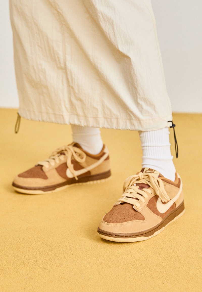 Tannfarbene und braune Wildledersneaker mit strukturierten Einsätzen, kontrastierenden Schnürsenkeln und einem weißen Swoosh-Logo, kombiniert mit weißen gerippten Socken.