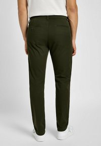 Pantalones verde oliva, ajustados, hechos de una tela suave, con dos bolsillos traseros con botones y un acabado liso y limpio.