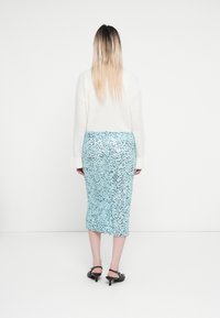Leichtes, gestricktes weißes Sweatshirt mit weit ausladenden Bündchen, kombiniert mit einem taillierten, knielangen Rock in Blau mit einem verstreuten Paillettenmuster.