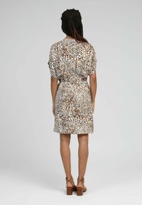 Robe à manches courtes avec une base blanche, ornée d'un imprimé léopard brun et noir. Taille élastique, longueur jusqu'aux genoux, associée à des sandales à talons marron.