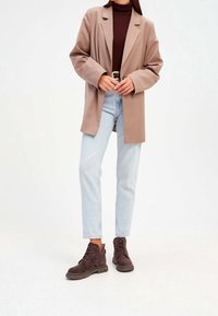 Beige bleiseri, ruskea poolopaita, vaaleansiniset farkut ja tummanruskeat nauhaketjut. Bleiserissä on rento malli ja leikatut läpät.