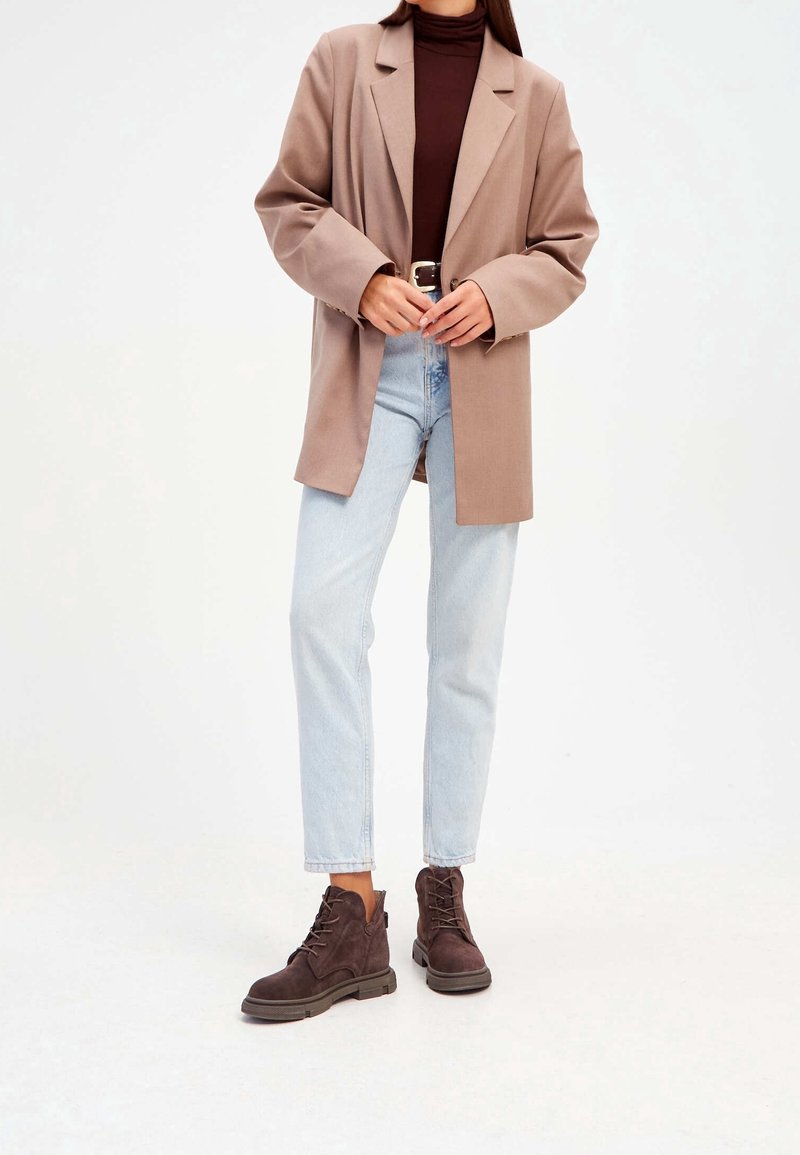 Beige bleiseri, ruskea poolopaita, vaaleansiniset farkut ja tummanruskeat nauhaketjut. Bleiserissä on rento malli ja leikatut läpät.