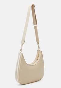 Beżowa torebka na ramię o zakrzywionym kształcie, z gładką fakturą, regulowanym paskiem, złotymi akcentami i zamykaną na zamek kieszenią po bokach.
