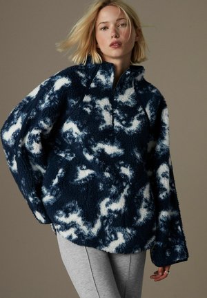 Marineblauwe en witte fleece pullover met een hoge kraag, ritssluiting en abstract wolkenpatroon. Heeft een ontspannen pasvorm en een gestructureerde stof.
