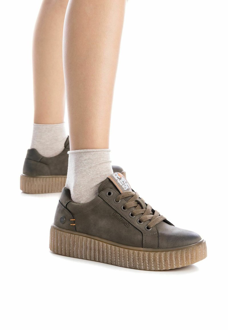 Zapatillas bajas de ante marrón con suela translúcida acanalada. Presentan puntera redonda, cordones y logotipo en la lengüeta. Llevadas con calcetines gris claro.