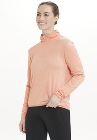 Letvægts, langærmet, lynlåset pullover i strukturfiber i koralfarve. Har en stående krave og en afslappet pasform. Kombineret med sorte leggings.
