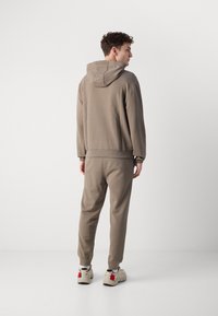 Sudadera kaki și pantaloni joggers cu o croială lejeră. Material moale, glugă și manșete elastice. Încălțămintea are o bază neutră cu accente roșii.