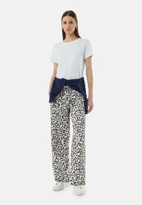 Maglietta bianca a maniche corte abbinata a pantaloni larghi con stampa leopardata. Un sudore blu navy è annodato in vita e le sneakers bianche completano il look.