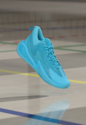 Chaussure de sport bleu clair en mesh et suède, avec un bout arrondi, des lacets plats et une semelle texturée distinctive, suspendue au-dessus d'un sol de salle de sport.
