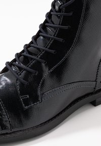 Bottines noires à lacets, brillantes, présentant une surface texturée, des accents en cuir lisse et une semelle en caoutchouc robuste. Couture détaillée visible.
