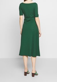 Grönrandig klänning med korta ärmar, båturringning och en flödande A-linjeform. Strukturerad tyg med detalj på sidosal.