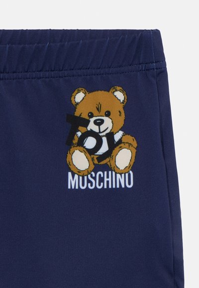 Bañador de color navy con un gráfico de un oso de peluche marrón y el texto "Toy" y "Moschino" en blanco. Fabricado con material suave y flexible.