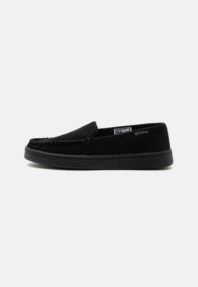 Chaussure décontractée noire slip-on avec un design moc toe cousu, un panneau latéral matelassé, une semelle en caoutchouc et une petite étiquette de marque à l'intérieur et sur le côté.