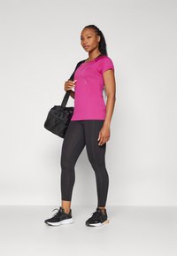 Rózsaszín sport póló rövid ujjakkal, fekete leggings-szel és fekete sportcipővel párosítva. Egy fekete sporttáska van a vállon.