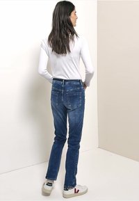 Jeans di denim blu a taglio slim con cuciture a contrasto, dotati di due tasche posteriori. Abbinati a una maglia bianca a maniche lunghe e sneaker bianche.