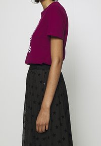 Fuchsia bomullströja med korta ärmar, kombinerad med en svart plisserad kjol med stjärnmönster och en texturerad midjeband.