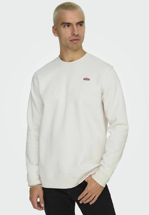 Witte crewneck sweatshirt van een katoenmix met ribgebreide manchetten en zoom. Bevat een klein rood logo-opdrachtje op de linker borst. Zwarte jeans worden erbij gedragen.