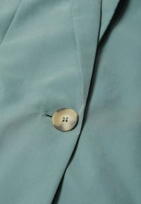 Tissu bleu clair avec un seul bouton rond beige cousu à côté d'une boutonnière sur un vêtement plié.