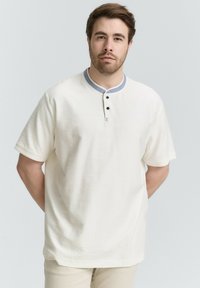 Weißes kurzärmliges Henley-Shirt mit grauem Kragen, drei schwarzen Knöpfen und einem kleinen mehrfarbigen Detail unter den Knöpfen. Weicher Stoff.