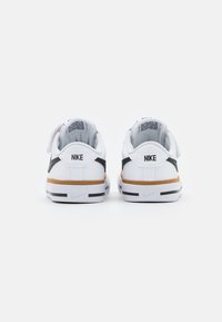 White Nike sneakers with black accents, leather material, rounded shape, and a tan rubber sole. Features a logo at the back.