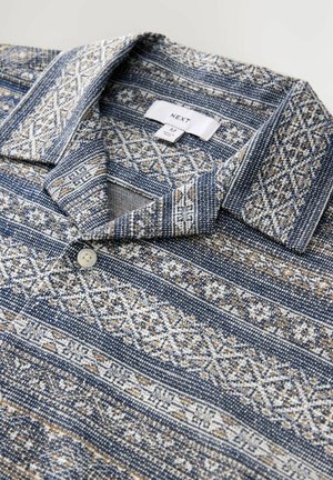 Blaues Poloshirt mit Muster und Kragen, das aufwendige geometrische Designs in Creme und Beige zeigt und eine Knopföffnung am Hals hat.