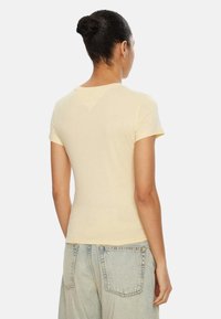 Camiseta de manga corta de color amarillo claro, fabricada con un tejido suave, con escote redondo y diseño ajustado, vista desde atrás.