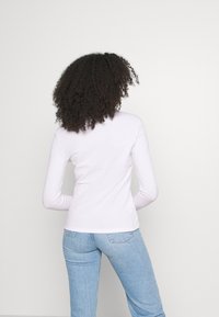 Långärmad, figurnära topp i ljusrosa bomull, med rund halsringning och slät yta, tillsammans med ljusblå denimjeans.