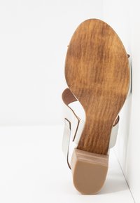 Sandalo bianco con tacco in legno, dotato di suola testurizzata e cinturini regolabili. Il tacco ha una finitura in legno lucido di colore marrone chiaro.