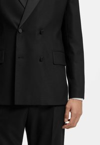 Giacca da smoking nera doppiopetto realizzata in tessuto texturizzato. Caratterizzata da due tasche frontali, bottoni neri e rever in satin.