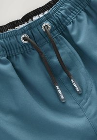 Short de bain en tissu bleu-vert avec une taille élastique, un cordon de serrage noir et des accents en caoutchouc. Texture lisse avec des détails cousus.