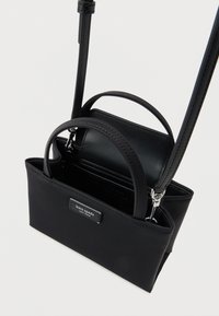 Μαύρη τσάντα Kate Spade New York με δύο λαβές και αποσπώμενο λουράκι ώμου σε απλό φόντο.