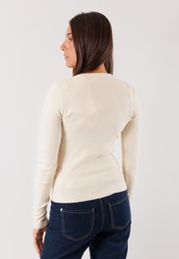 Top a maniche lunghe di colore crema a coste con un design aderente. Abbinato a jeans in denim scuro, che mostrano una texture liscia e uno stile classico.