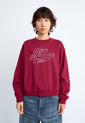 Sweatshirt bordeaux avec un col rond côtelé, des manches longues et un grand logo blanc "New Balance Athletics" sur le devant. Texture douce.
