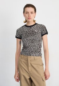 Tričko s krátkými rukávy v leopardím vzoru s černým žebrovaným límcem a rukávy. Měkká tkanina s přiléhavým střihem, v kombinaci s béžovými kalhotami.